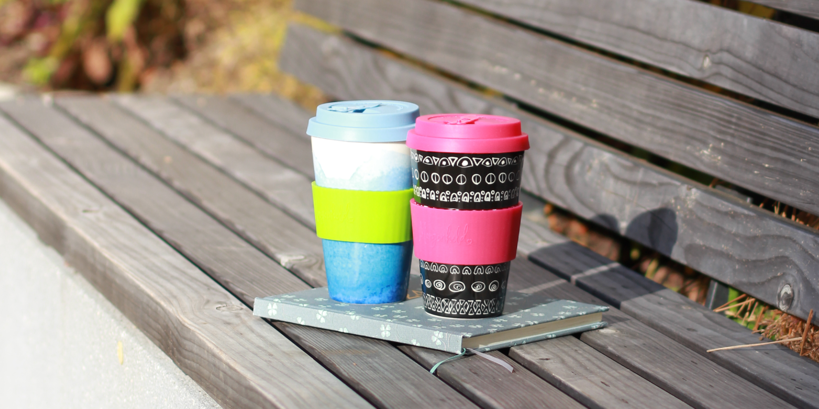 Morgenheld Coffee to Go Becher Hili Blue und Balcky Berry auf einer Parkbank