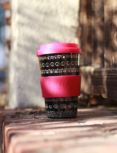 Wiederverwendbarer Becher to Go mit pinkem Deckel und Griffband auf Holzbank im Herbstlicht – nachhaltiger Kaffeegenuss mit Designanspruch.