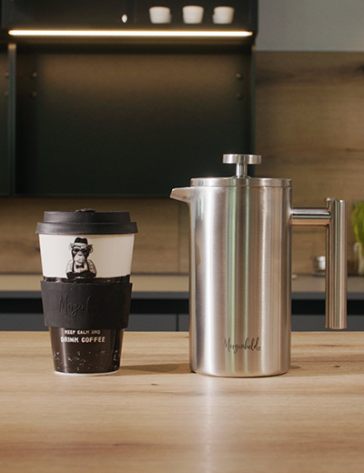French Press aus Edelstahl von auf dem Küchentisch – stilvolle Stempelkanne für aromatischen Kaffeegenuss mit einem Monkey Coffee to Go Becher von Morgenheld bereit für den ersten Kaffee am Morgen